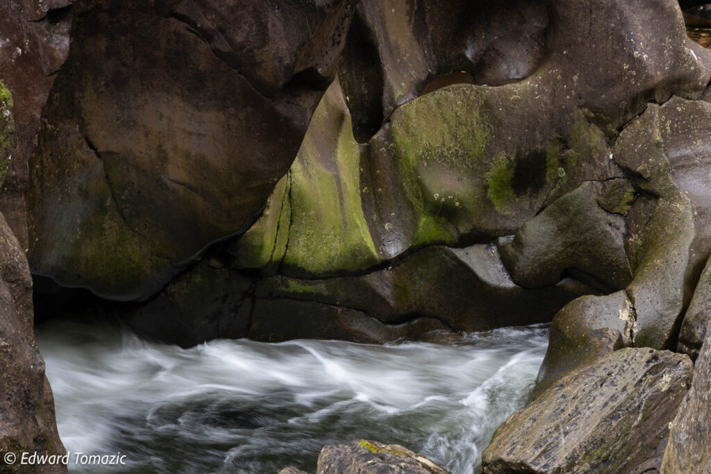 Smooth water flows through sculpted rock formations with moss textures in a narrow natural gorge.